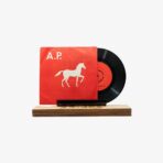 Red vinyl record and red album cover with a white horse silhouette and the letters A.P. on a wooden display stand.