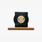 Black vinyl record mounted on a dark display stand atop a wooden base, shown head-on with the label visible.