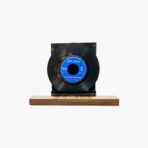Black vinyl record mounted on a dark stand placed on a light wooden base, blue label visible at center, vintage look.