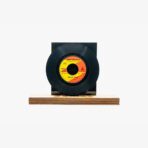 Vinyl record mounted on a black square pedestal with a wooden base, label orange and yellow at center.