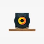 Black vinyl record on a wooden display base with an orange-yellow label on the center.