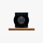 Black vinyl record mounted on a dark rectangular block set on a wooden platform, minimalist display art piece