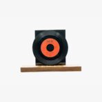 Vinyl record mounted on a black stand with an orange label, resting on a wooden base.