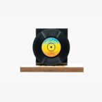 Black vinyl record on a wooden display stand with a dark backboard behind it.