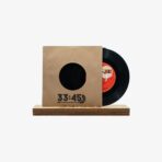 Vinyl record partially removed from a brown cardboard sleeve with a round cutout, placed on a wooden stand. The sleeve shows '33:45' text at the bottom left.