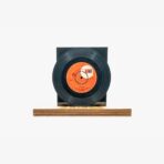 Black vinyl record with an orange label mounted on a black display stand atop a wooden base.