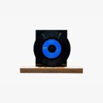 Black vinyl record mounted on a wooden block pedestal with a blue label visible at the center.