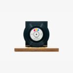 Black vinyl record mounted on a wooden pedestal with a dark backing, set against a white background.
