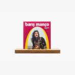 Barış Manço album cover with the singer in ornate black clothing inside a yellow-arched frame on a pink background