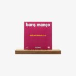 Barış Manço vinyl album cover on a wooden pedestal, pink background with bold white title and yellow subtitle 'DAĞLAR DAĞLAR (1-2)'.