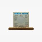 Vinyl record sleeve titled 'BEHIYE AKSOY' mounted on a wooden display stand with a circular cover hole in the center, white background