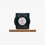 Black vinyl record mounted on a dark display with a wooden base on a white background.