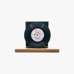 Black vinyl record mounted on a wooden base with a dark rectangular backing behind it.