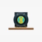 Black vinyl record mounted on a dark square backing atop a wooden base (display setup).