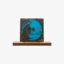 Album cover: blue circular silhouette of a face on a black background, resting on a wooden stand/shelf edge