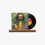Vintage vinyl record with Cem Karaca album cover featuring a bearded man with glasses in a yellow sweater and blue jacket, on a wooden stand.