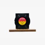 Black vinyl record mounted on a rectangular black display block atop a wooden base. (Studio shot)