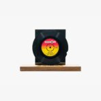 Black vinyl record mounted on a wooden base with a colorful red‑yellow center label on display.