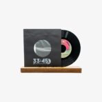 Black vinyl record partially pulled from a dark sleeve with a circular window, resting on a wooden display stand.