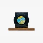 Black vinyl record mounted on a black display, resting on a wooden base/stand.