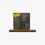 Vintage album cover mounted on a wooden display stand against a light gray background.