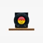 Black vinyl record displayed on a wooden stand with a colorful label in the center.
