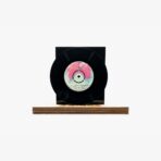 Black vinyl record displayed on a wooden pedestal with a colorful center label visible