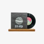 Vinyl record partially pulled from a gray sleeve with a circular cutout, resting on a wooden stand, showing '33:45' on the sleeve.