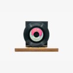 Black vinyl record mounted on a wooden stand with a black backing against a white background.