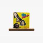 Yellow album cover with four band members’ portraits on a bright background, placed on a wooden base.