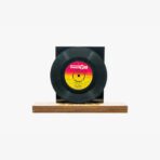Black vinyl record mounted on a dark square backing atop a wooden display base.