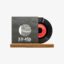 Black vinyl record partially slid out of a gray sleeve with a circular window, placed on a wooden base; sleeve shows '33:45'.