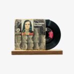 Vinyl record with a worn artwork sleeve featuring a portrait, resting on a wooden stand against a light background.