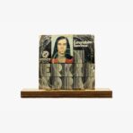 Vintage distressed album/poster cover mounted on a wooden pedestal, featuring a portrait and bold typography.