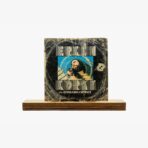 Album cover displayed on a wooden stand: a scratched black circular design with geometric striped text framing a blue-tinted portrait in the center. Bottom reads ‘509-ESTARABIM • SEVINCE’ (retro record sleeve).