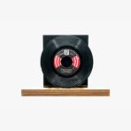 Black vinyl record mounted on a wooden base with a dark rectangular backdrop, set against a white background.