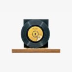 Vintage black vinyl record on a light wooden display stand against a white background, label visible in center.