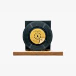 Black vinyl record mounted on a wooden base against a light background, displayed like a collectible.