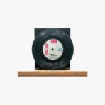 Black vinyl record mounted on a black square display block, resting on a wooden base/stand.