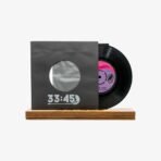 A black vinyl record partially pulled from a gray sleeve with a circular cutout, resting on a wooden display base, showing '33:45' on the sleeve edge.
