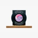 Black vinyl record mounted on a wooden base with a pink center label.
