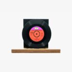 Black vinyl record mounted on a wooden rectangular base with a bright orange label facing outward.