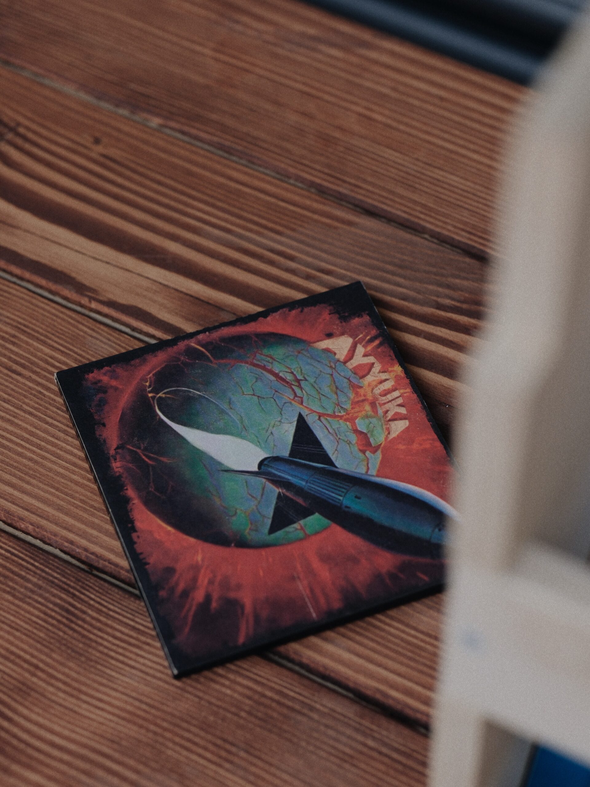 Colorful space-themed book cover with a rocket illustration lying on a wooden floor, photographed at an angle with a blurred foreground edge.