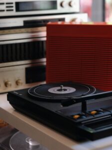 Turntable spinning a vinyl record in the foreground with a large red speaker and vintage audio gear in the blurred background.