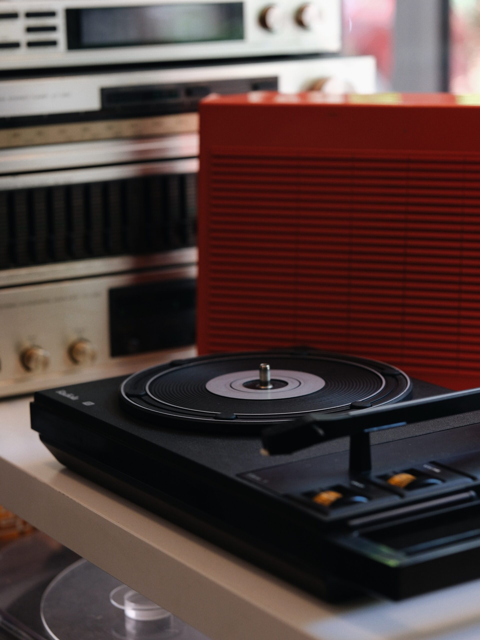 Turntable spinning a vinyl record in the foreground with a large red speaker and vintage audio gear in the blurred background.