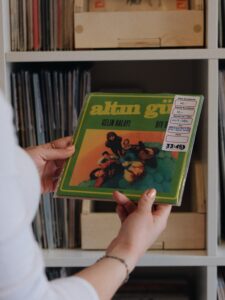 Person holding a green vinyl record in a clear sleeve near a shelf of records.