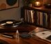 Turntable on a wooden desk with a spinning vinyl, surrounded by stacked records, a small plant, and a warm desk lamp.